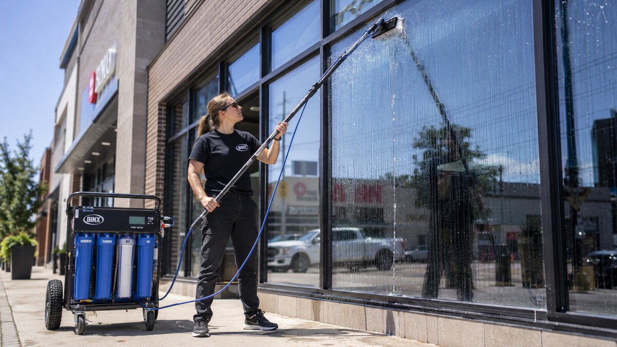 Binx technician using a water-fed pole with reverse osmosis purified water on a sunlit commercial storefront window &mdash; Binx Professional Cleaning